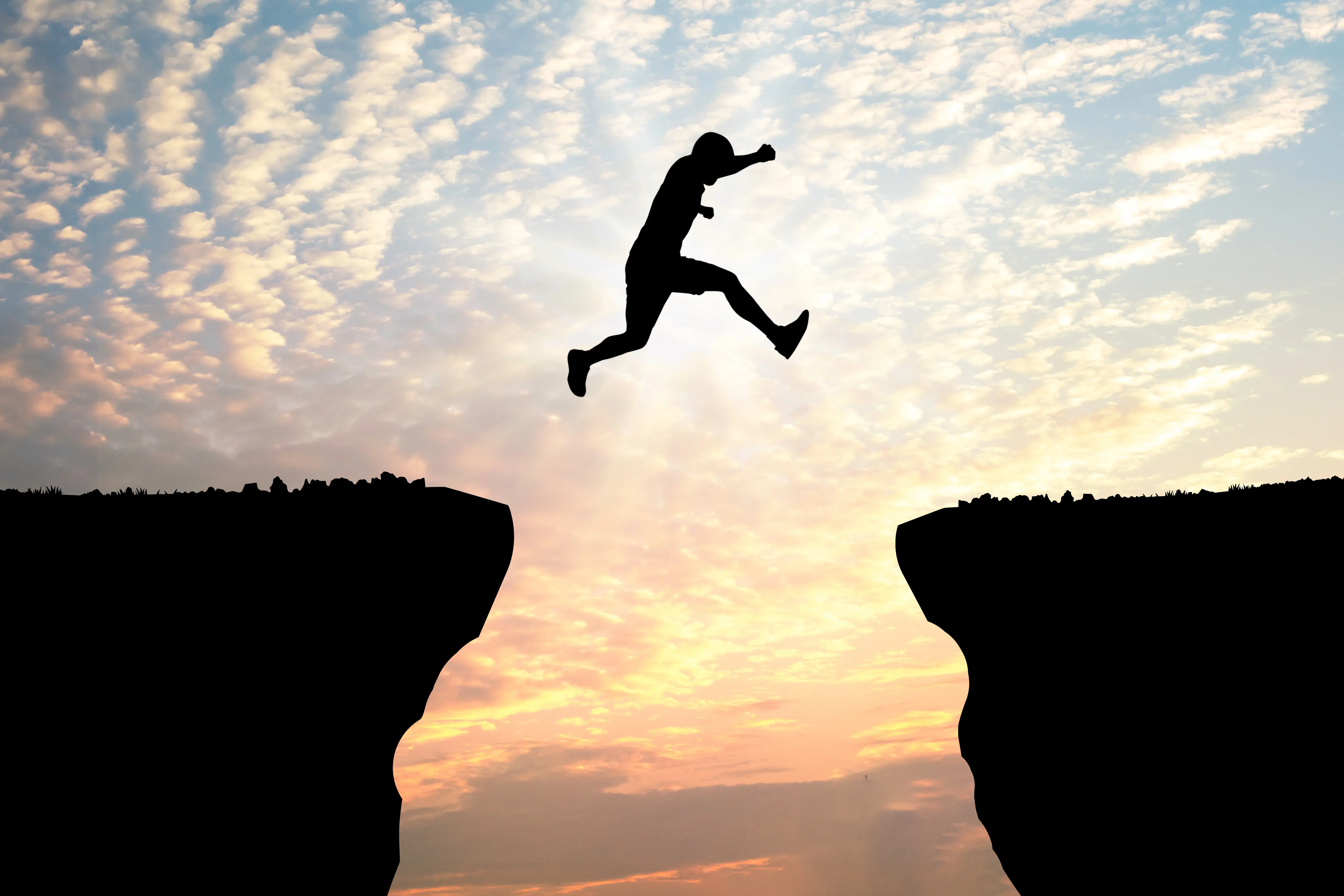 A traveller leaping between rocks above the ocean.